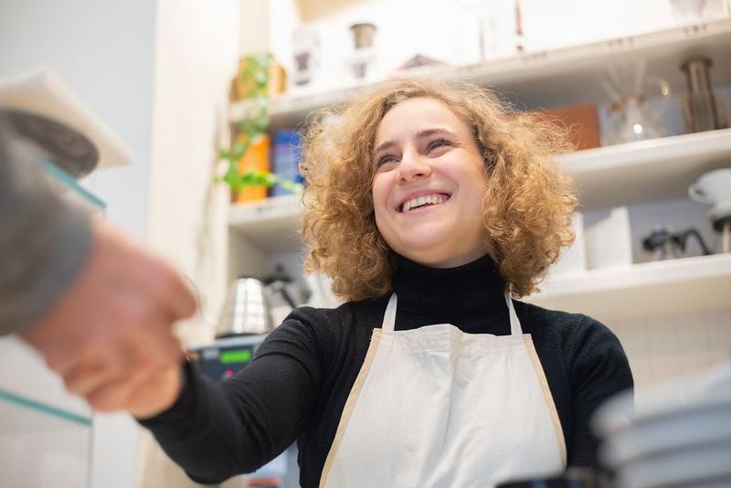 La dueña de un café le da la mano a un cliente por encima del mostrador