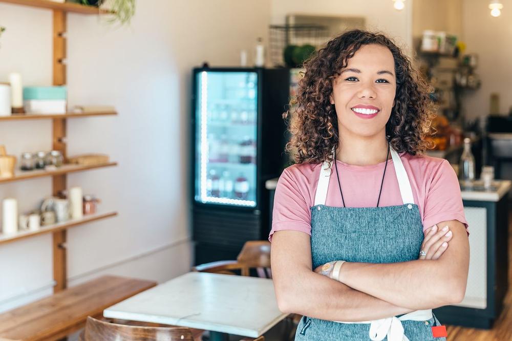 La dueña de un café, de brazos cruzados y sonriendo en su local