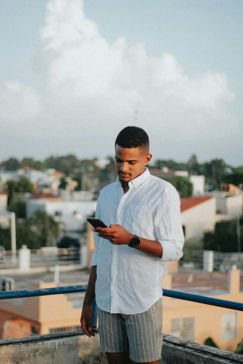 Un joven escribe en su teléfono en una azotea, con la ciudad detrás
